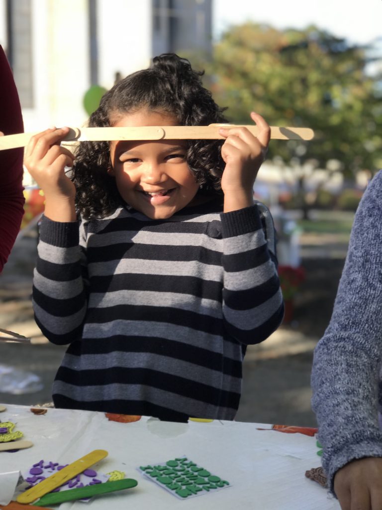 A little girl displays her craft proudly at an outdoor community event